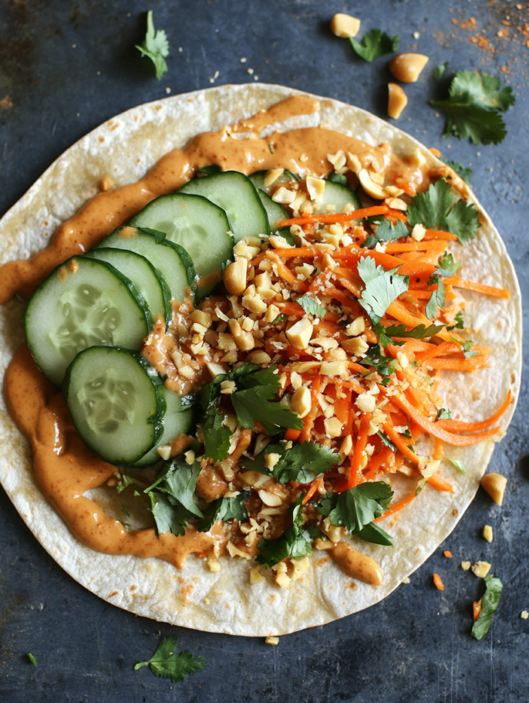 A vegan peanut crunch wrap filled with cucumber, carrots, bell peppers, and cilantro coated in peanut sauce, a fun low-carb wrap idea with a healthy crunch.