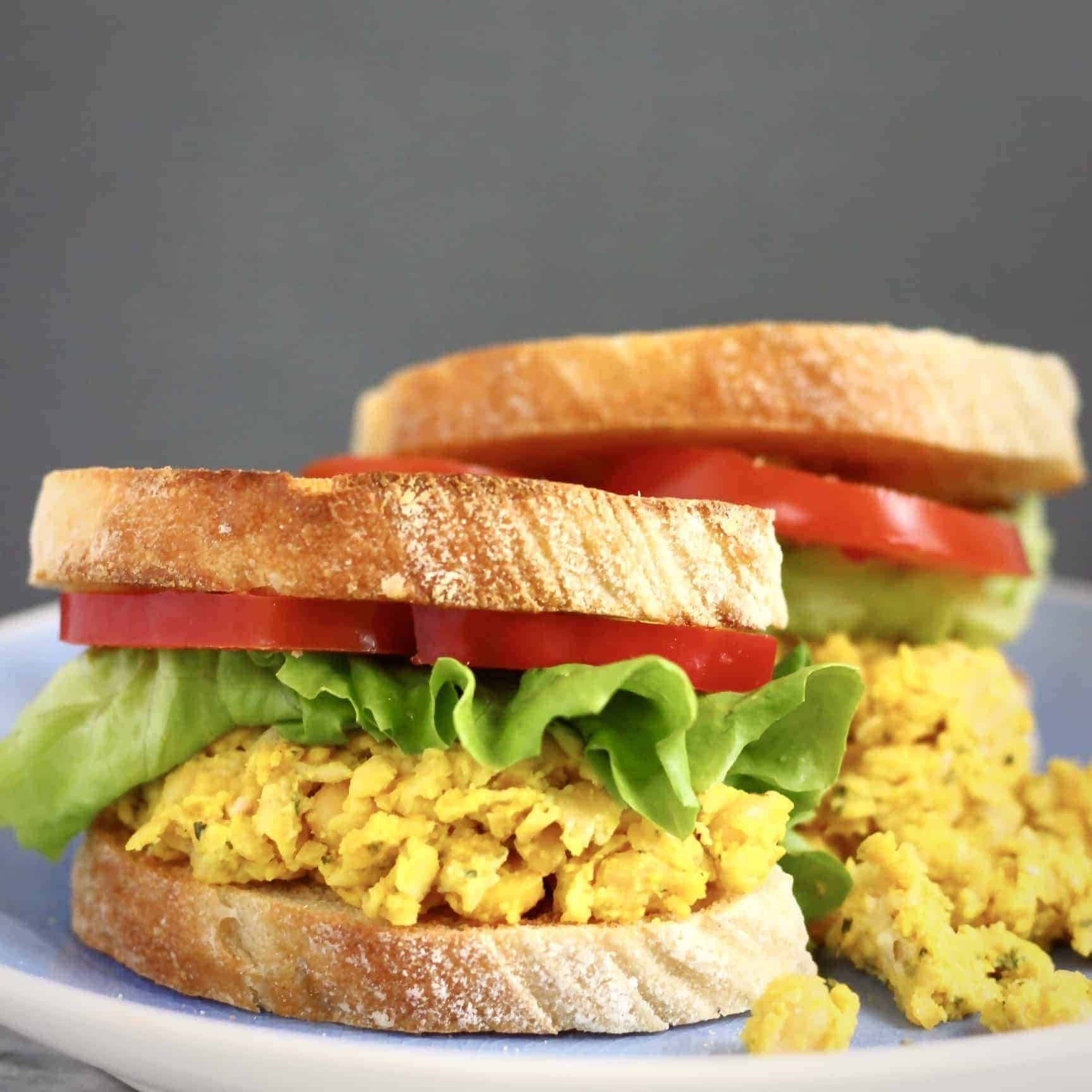 Curried chickpea salad sandwich with creamy filling, greens and pickled onion