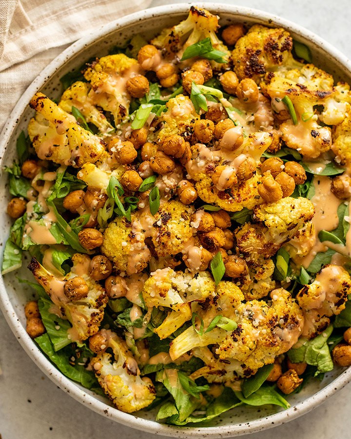 Golden roasted cauliflower, chickpeas and autumn vegetables on a tray with tahini sauce