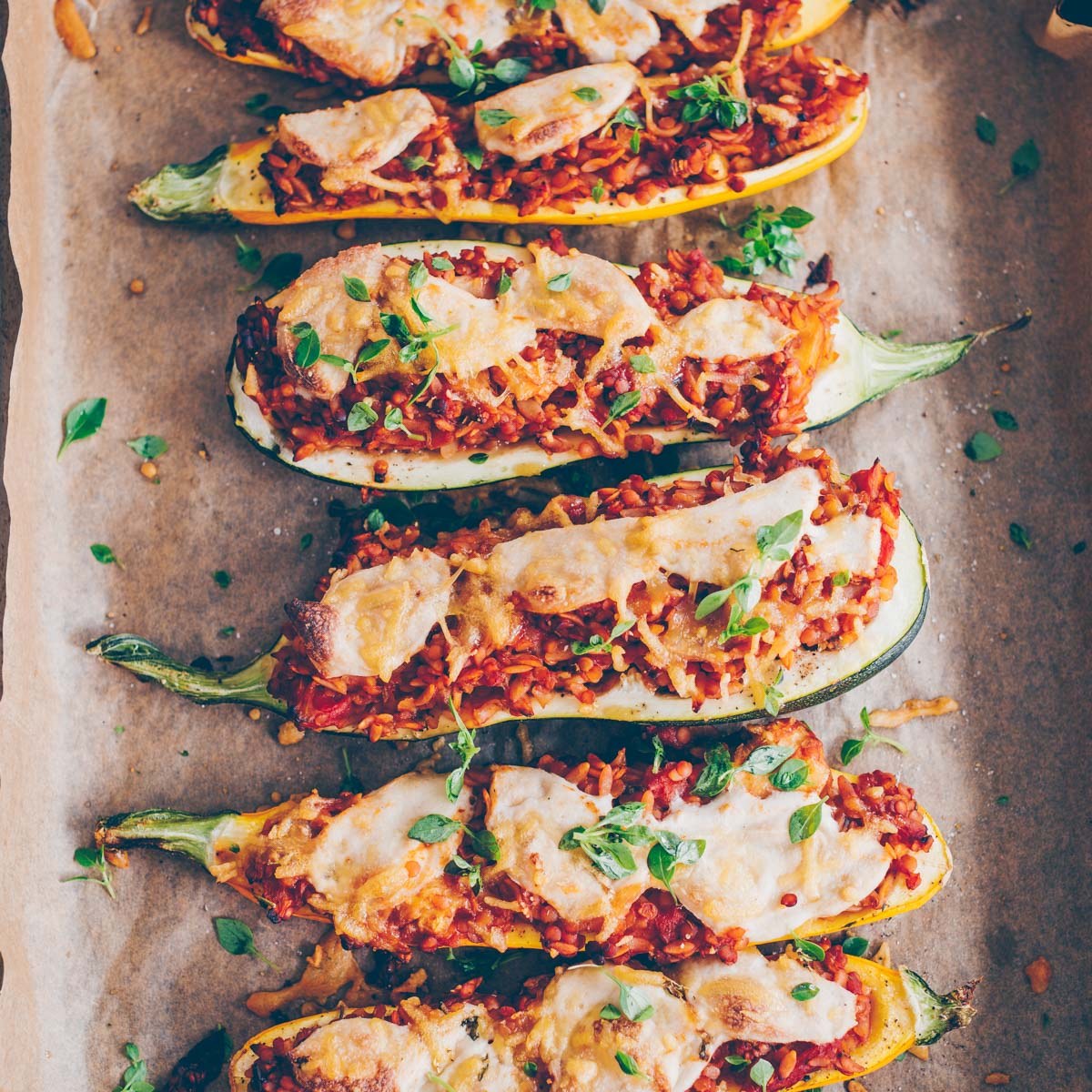 Baked vegan zucchini halves filled with lentils and small pasta in tomato sauce