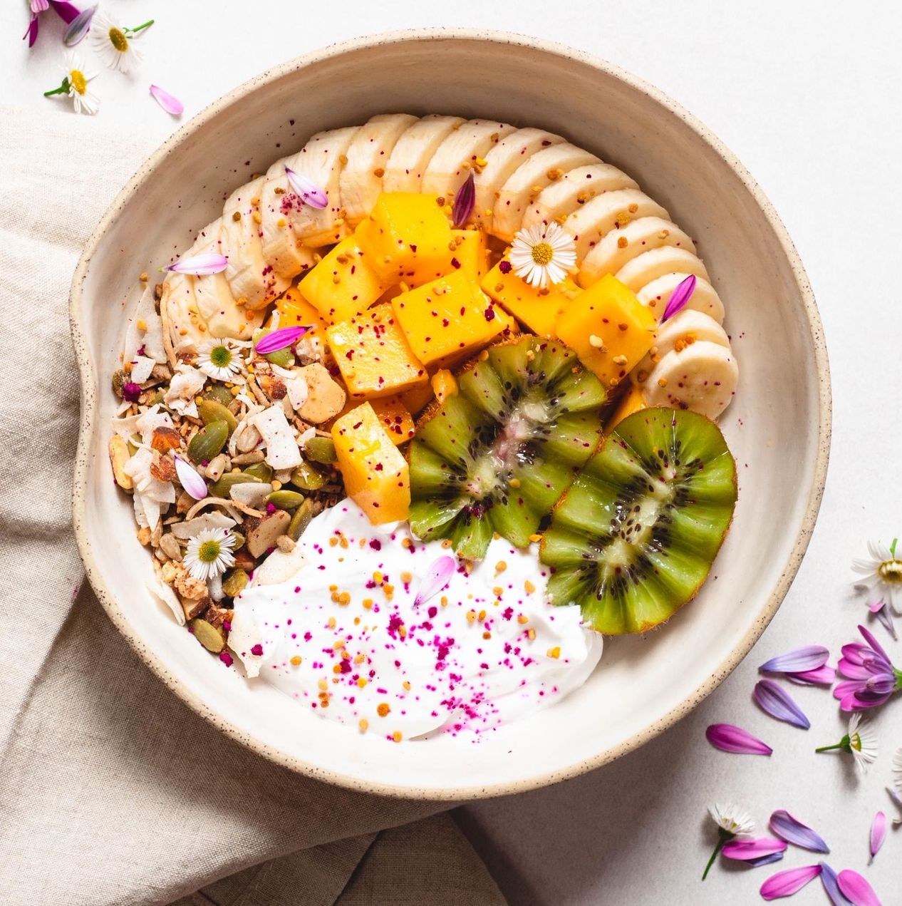 Coconut yoghurt bowl topped with granola, banana, mango, and kiwi