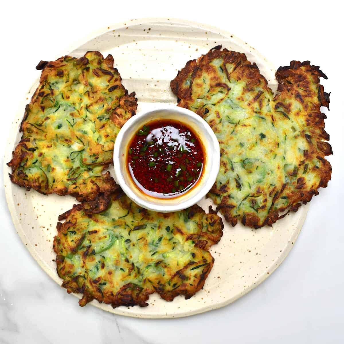 Three crispy vegan zucchini fritters served with dipping sauce