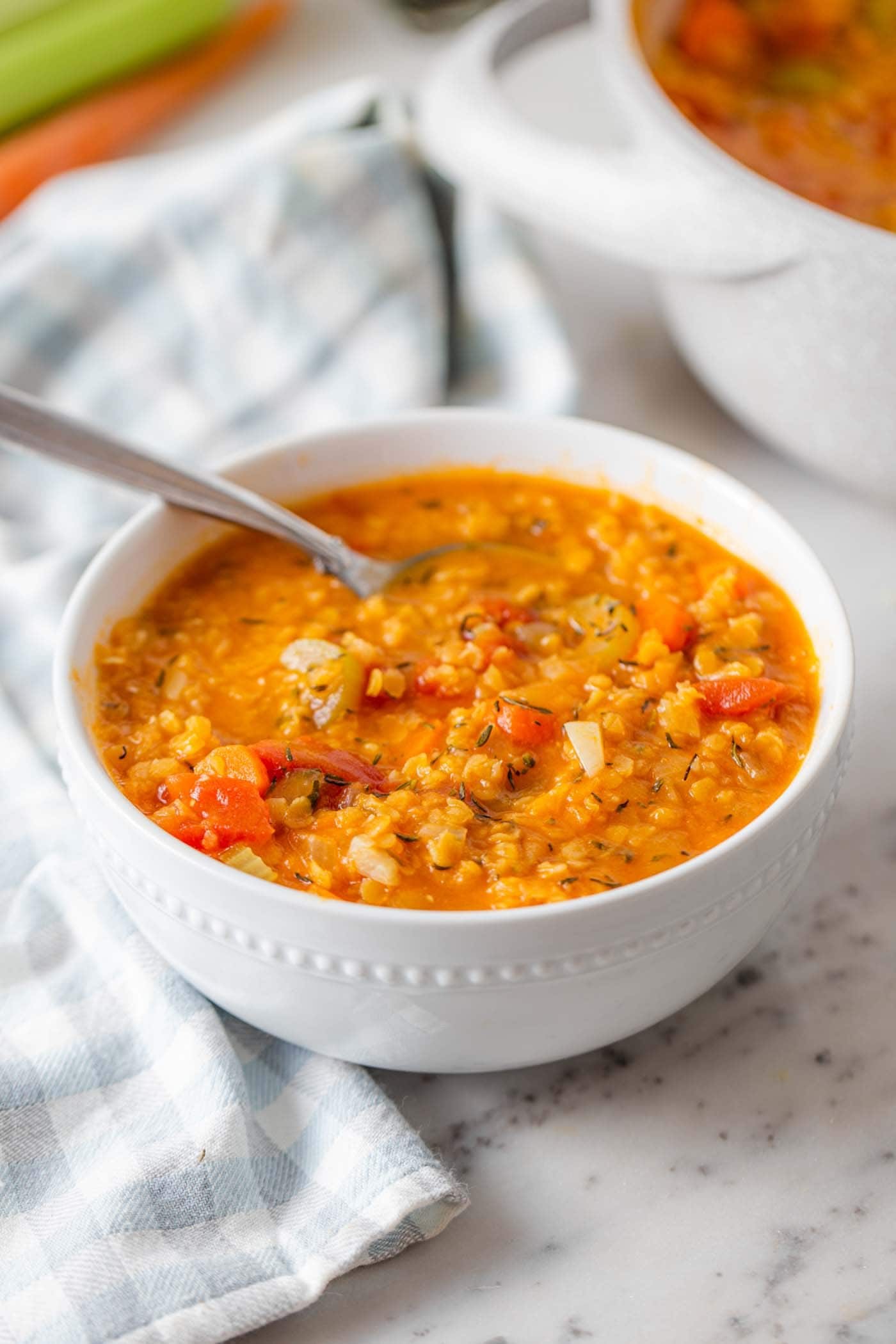 Bowl of vegan red lentil tomato soup with vegetables and herbs