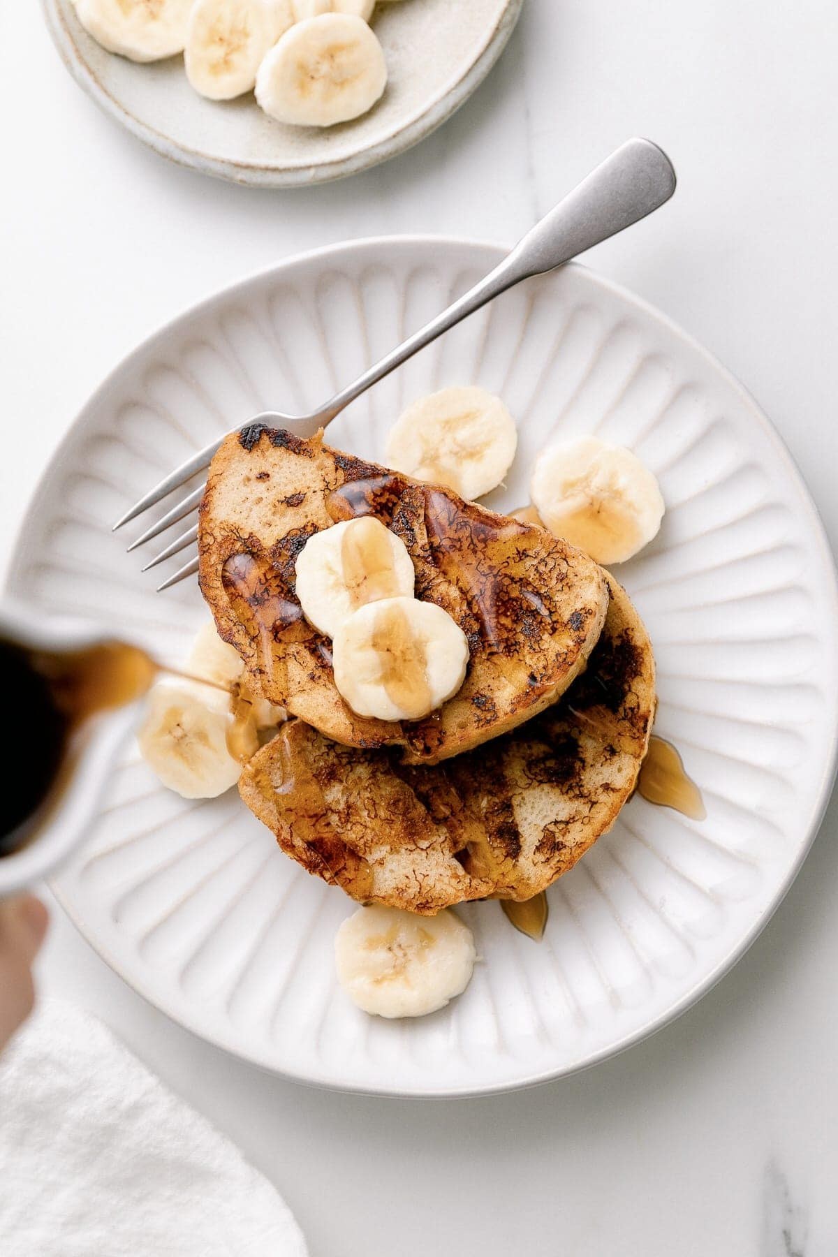 Stacked vegan banana French toast topped with banana slices and maple syrup