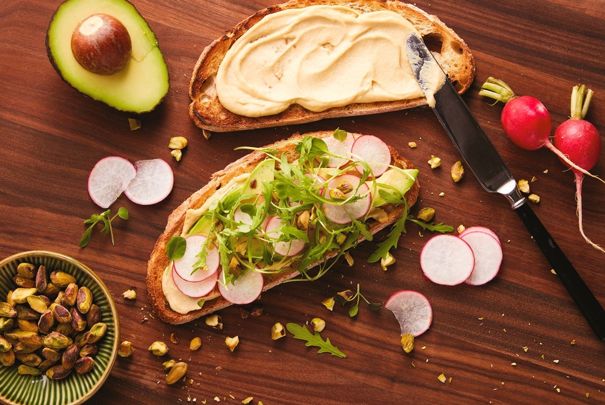 Vegan hummus toast topped with avocado, greens, radish and crunchy seeds