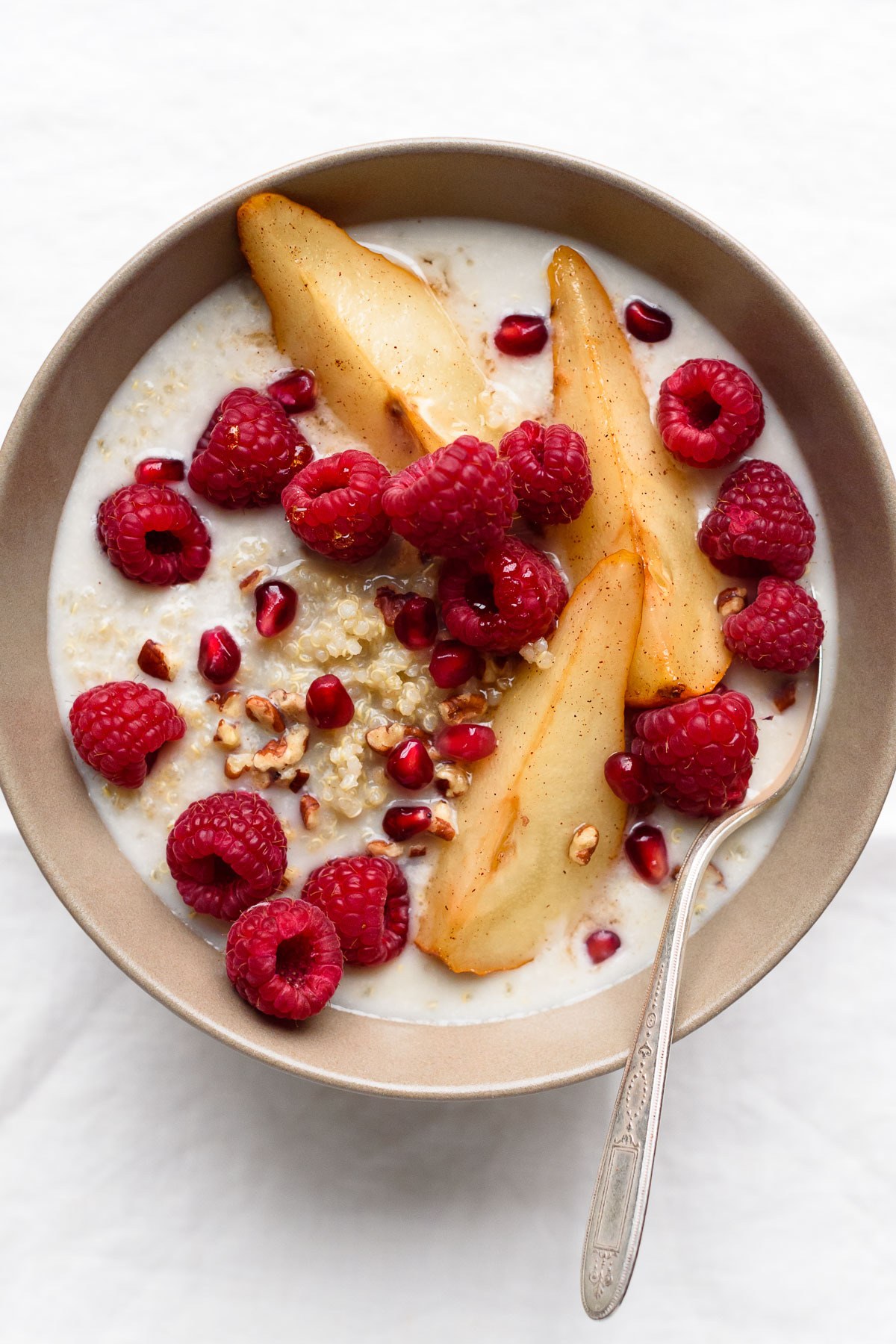 Warm quinoa breakfast grain bowl topped with fanned pear slices and chopped pecans