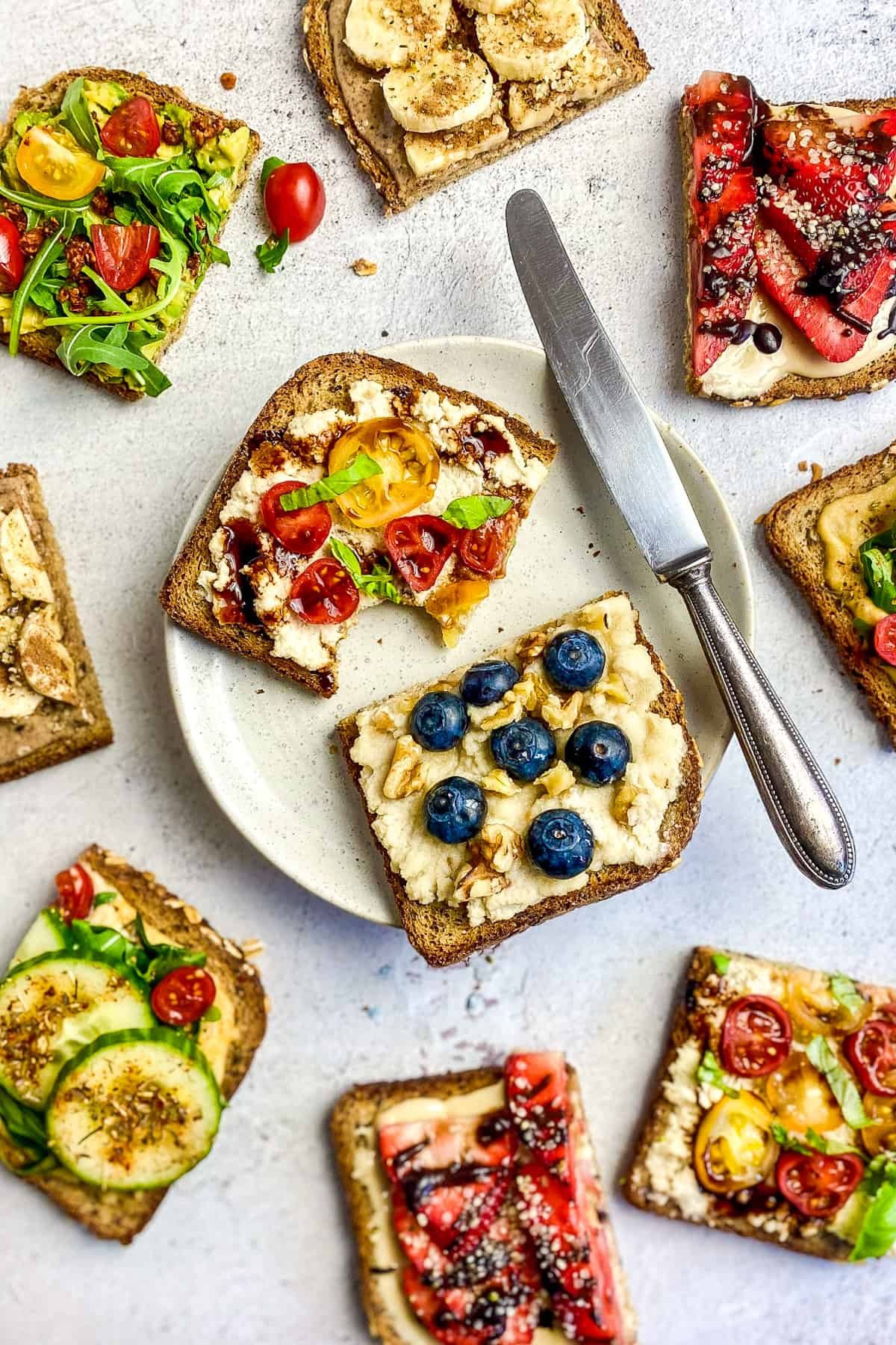 Whole grain vegan toast topped with nut butter, sliced fruit, dates, blueberries, and seeds