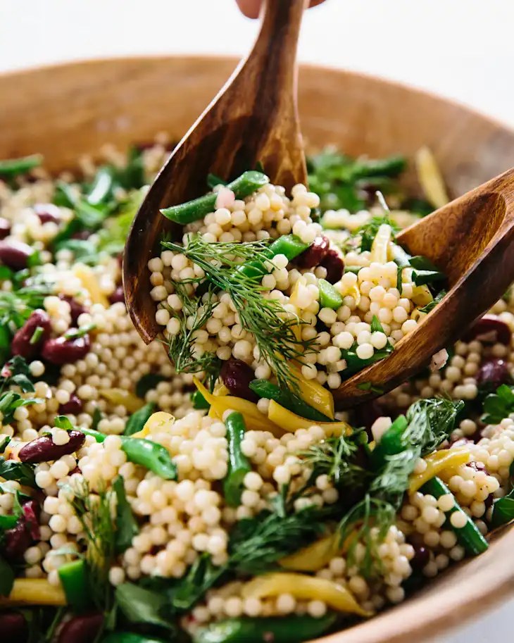Close-up of pearl couscous salad with kidney beans, green beans, yellow beans, dill and parsley in a wooden bowl